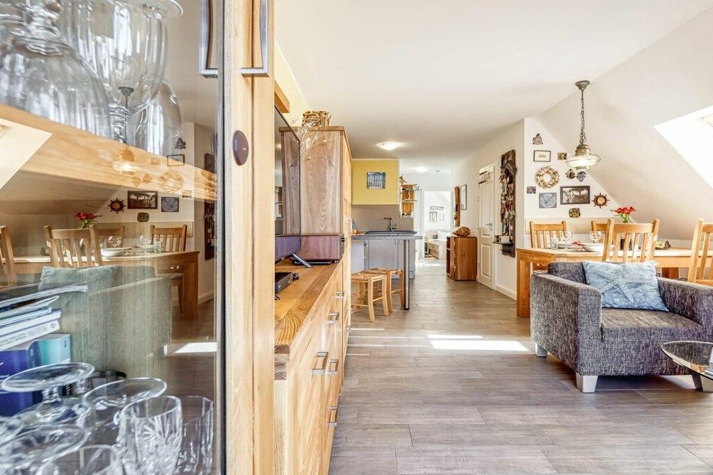 Ein großzügiger Wohnbereich mit Sofa, Esstisch und Stühlen. Im Hintergrund ist eine Küche erkennbar.