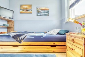 Une chambre à coucher avec un lit, une commode en bois, une étagère avec un bol, et deux tableaux accrochés au mur.