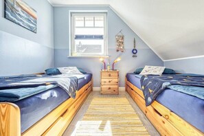Une chambre avec deux lits, une fenêtre, une commode en bois et un élément décoratif suspendu.