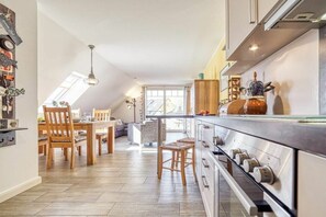 A modern kitchen with a central island, wooden chairs, and a dining area with a table and chairs. - Holiday apartment with 1 bedroom (Seeheilbad Zingst)