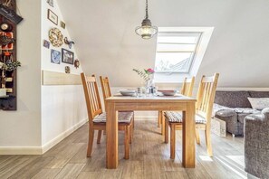 A dining area with a wooden table and chairs, a chandelier, and a window with a view. - Holiday apartment with 1 bedroom (Seeheilbad Zingst)