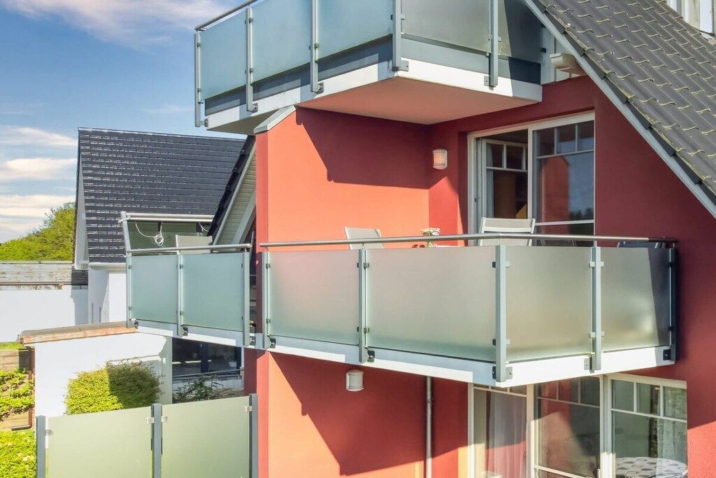 Ein mehrstöckiges Gebäude mit roter Fassade, einem Balkon mit Glasgeländern und einem sichtbaren Fenster.