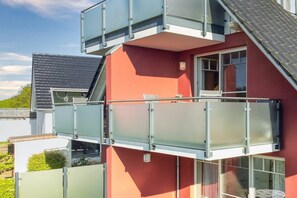 Un immeuble à plusieurs étages avec une façade rouge, un balcon doté de rampes en verre et une fenêtre bien visible.