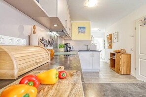 Une cuisine moderne avec un plan de travail en bois, une planche à découper avec des légumes, et une vue sur l’espace repas.