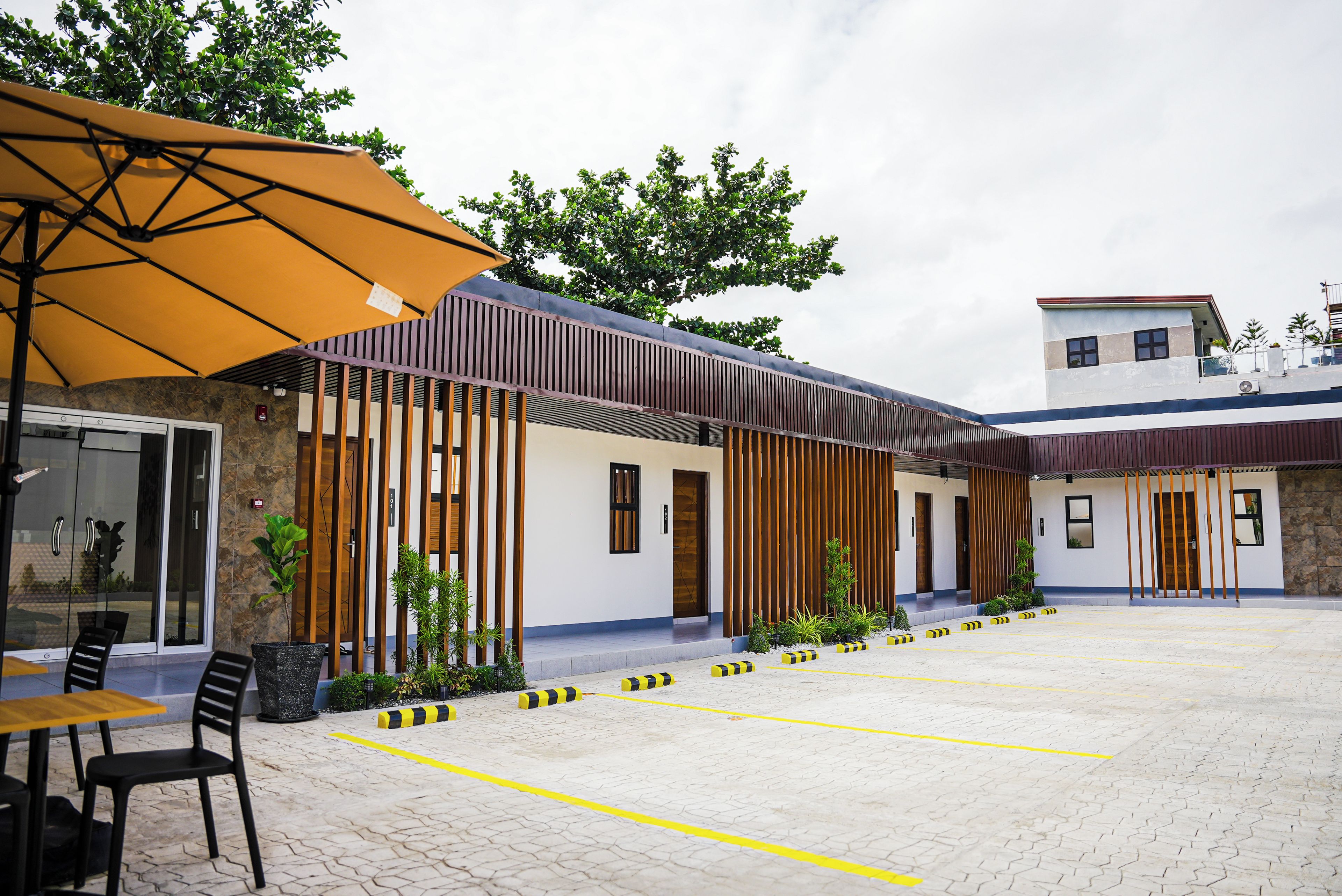 A covered outdoor seating area with tables and chairs, a yellow umbrella, and a building with vertical wooden slats.