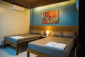 A hotel room with two single beds, a nightstand with a lamp, and a wall-mounted air conditioner.