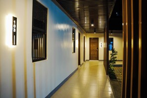 A hotel corridor with a tiled floor, a wooden door, and a small plant.