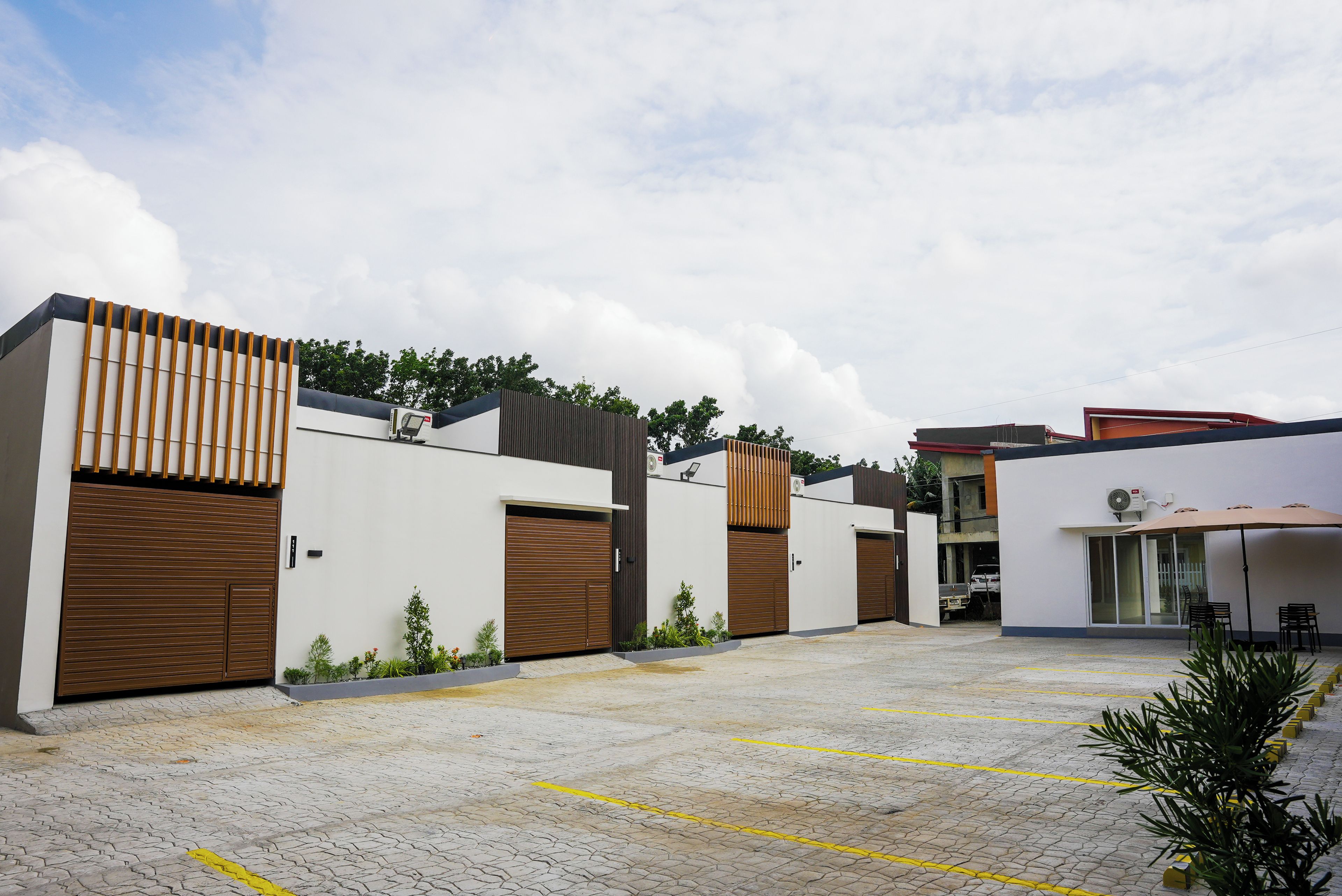 Un edificio moderno con puertas de madera grandes, un patio empedrado y una zona de estar cubierta.