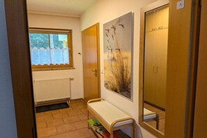 A hallway with a radiator, a window with a lace curtain, a bench, and a door with a mirror. - 2.3/T4 Holiday Park "Freesenbruch" (Zingst (Ostseeheilbad))