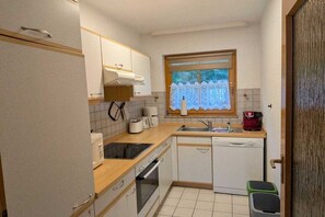 A compact kitchen with a stove, oven, sink, and a window with curtains. - 2.3/T4 Holiday Park "Freesenbruch" (Zingst (Ostseeheilbad))