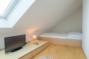 A bedroom with a sloped ceiling, a bed, a TV on a desk, and a lamp. - Residence Am Strand 6-82 (Seeheilbad Zingst)