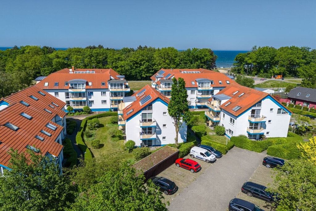 A residential complex with multiple two-story buildings, a parking area, and a view of the sea.