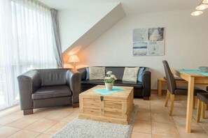 A modern living room with a sofa, a coffee table, and a dining area. - Residence Am Strand 6-82 (Seeheilbad Zingst)