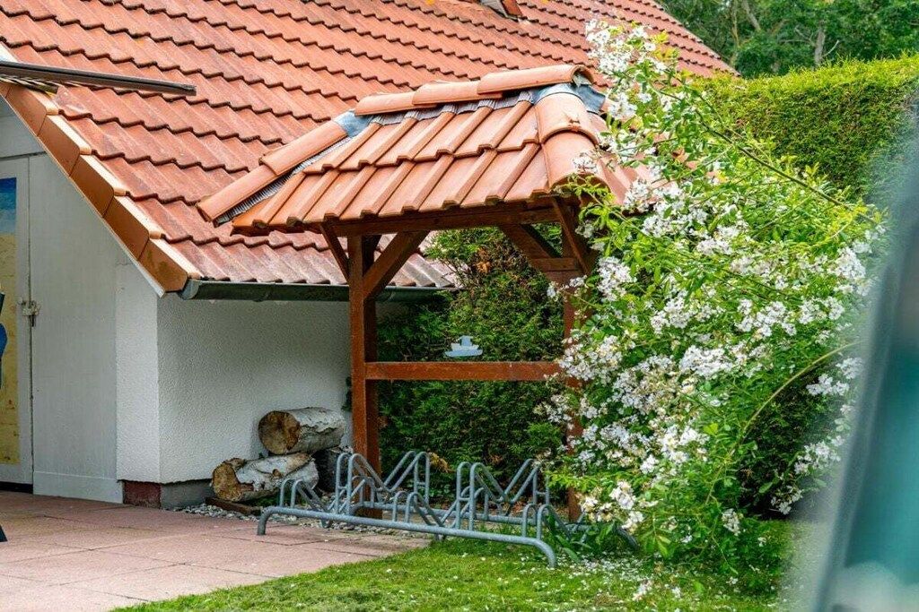 A building with a red-tiled roof, a wooden pergola, and a garden with white flowering plants.