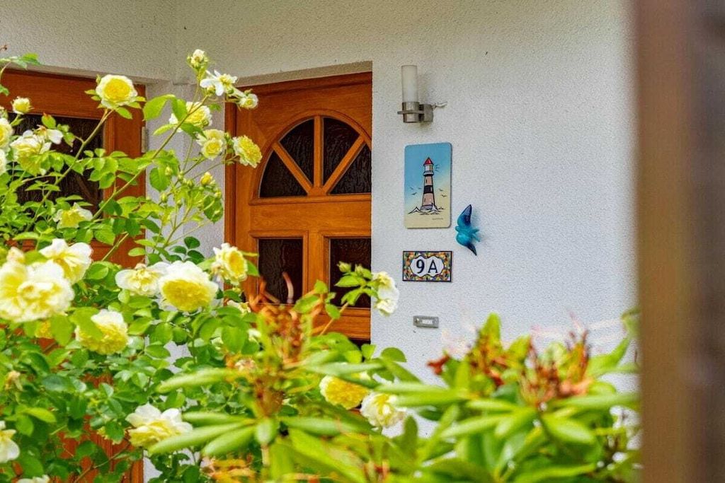 Una puerta de madera con un ventanal, una lámpara fijada a la pared y una pequeña placa con el número '9A'.