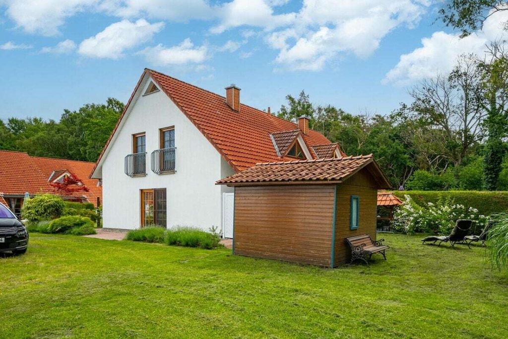A two-story house with a red-tiled roof, a small wooden structure, and a well-maintained lawn.