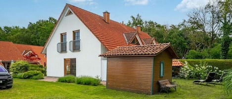 A two-story house with a red-tiled roof, a small wooden structure, and a well-maintained lawn.