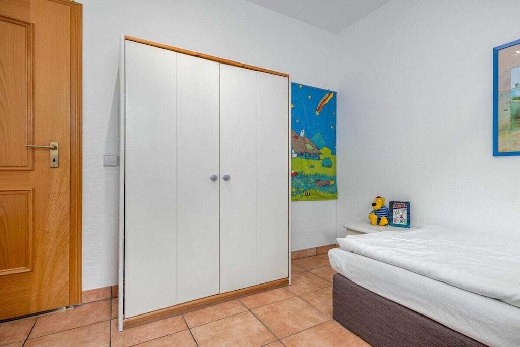 A bedroom with a bed, a wardrobe, a door, and a wall with a painting.