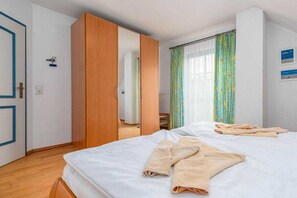 A bedroom with two beds, a wardrobe, and a window with curtains. - 11/T6 holiday home park “Freesenbruch” (Zingst (Ostseeheilbad))
