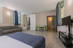 Quarto de hotel com cama, sofá, mesa de jantar com cadeiras, televisão e pequeno armário.