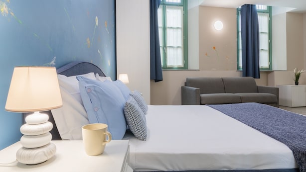 A hotel room with a bed, a bedside table with a lamp, a coffee cup, and a sofa. - Housing Giulia - Apartment 8 by Wonderful Italy (Turin)