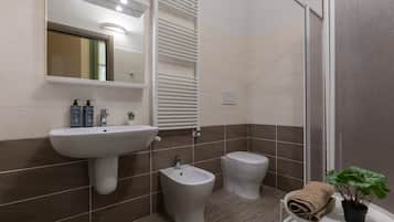 Ein modernes Badezimmer mit einem Standwaschbecken, zwei Toiletten, einem Bidet und einem Handtuchhalter mit einer Pflanze.