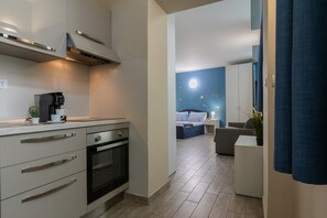 A modern kitchen with a built-in oven and a dining area with a blue wall and a bed.