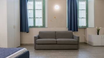 Una sala de estar moderna con un sofá gris, dos ventanas con cortinas azules, un mueble blanco pequeño y una lámpara fijada a la pared.