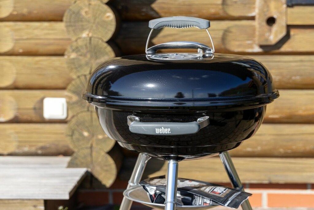 Ein tragbarer Weber-Grill mit Deckel und Bürste vor einem hölzernen Hintergrund.