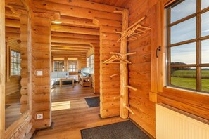 A log cabin interior with a wooden wall, a coat rack, a window with a view, and a door leading to another room. - Holiday home in Sassnitz/Rügen with sauna (Sassnitz\/Rügen)