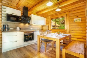 A wooden cabin interior with a kitchen, dining table, and a window with a view. - Holiday home in Sassnitz/Rügen with sauna (Sassnitz\/Rügen)