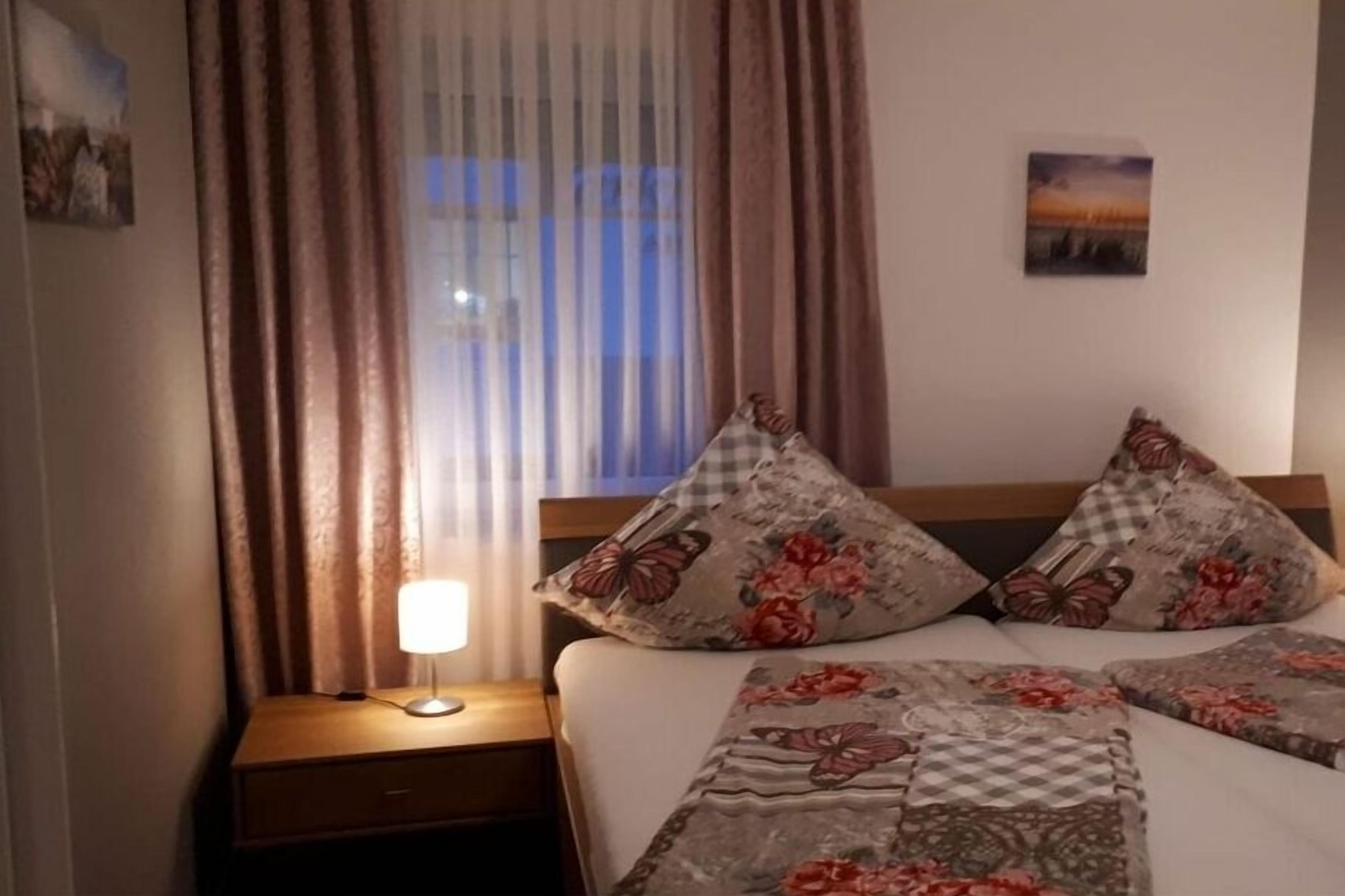 A hotel room with a bed, a nightstand, a lamp, curtains, and a wall-mounted picture.