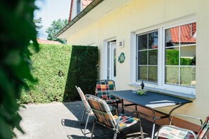 A patio with a table and chairs, a hedge, and a building with a number sign. - At the dike, house number 26 (Ostseebad Zingst a Darß)