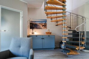 A spiral staircase with wooden steps and metal railings, a blue cabinet with a basket, and a framed picture on the wall. - At the dike, house number 26 (Ostseebad Zingst a Darß)