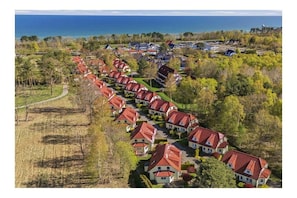A residential area with houses featuring red-tiled roofs, arranged in a linear pattern along a road, with a body of water in the background. - At the dike, house number 26 (Ostseebad Zingst a Darß)