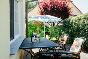 Eine Terrasse im Freien mit Tisch und Stühlen, bewölkter Himmel und ein Haus im Hintergrund mit roten Blättern.
