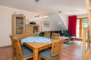 A dining area with a wooden table and chairs, a cabinet with glass doors, and a sofa in the background. - 4.6/T1 holiday home park “Freesenbruch” (Zingst (Ostseeheilbad))