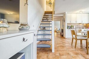 Eine Treppe führt zu einer Küche mit weißen Schränken und einem Essbereich mit Tisch und Stühlen.