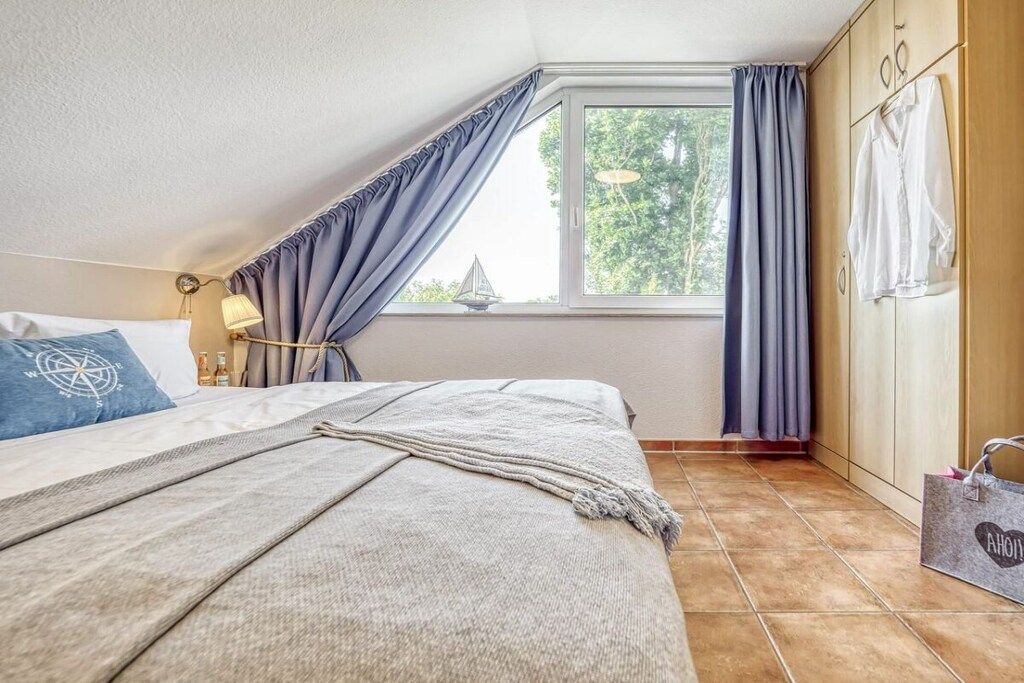 Une chambre à coucher avec un lit, une fenêtre avec des rideaux, une armoire et une table de chevet avec une lampe.