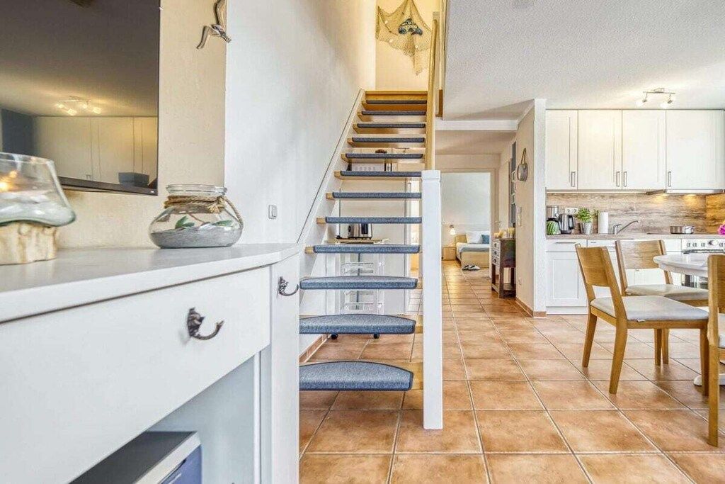 Un escalier menant à une cuisine avec des meubles blancs et un coin repas comprenant une table et des chaises.