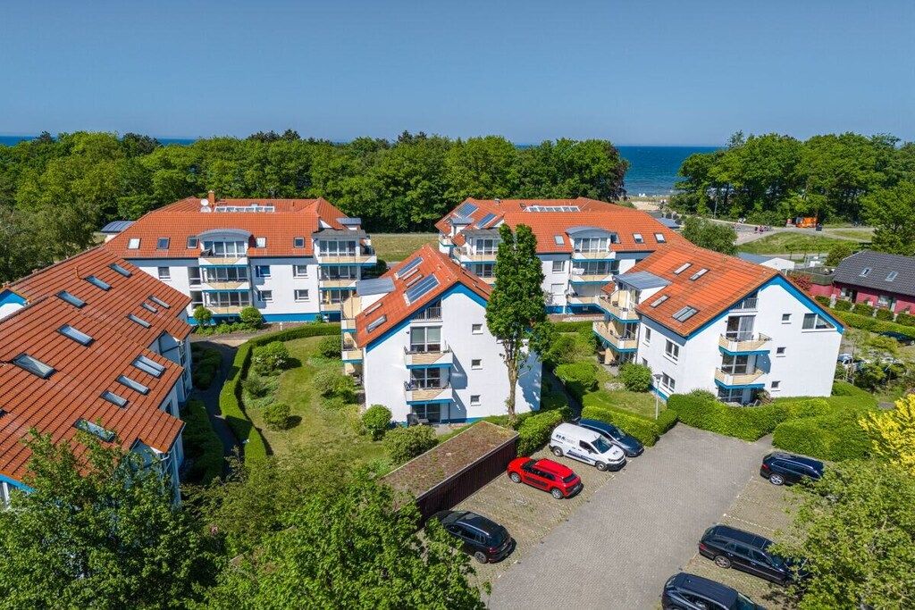 A residential complex with multiple two-story buildings, a parking area, and a view of the sea.