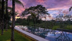 A pool with a clear view of surrounding trees and a sunset sky. - Villa Babadan (Badung)