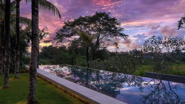A pool with a clear view of surrounding trees and a sunset sky. - Villa Babadan (Badung)