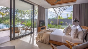 A bedroom with a large bed, a TV, and a view of an outdoor swimming pool and garden. - Villa Babadan (Badung)