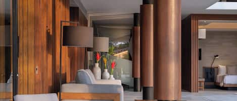 Un interior moderno con sofá, una mesa de centro y una lámpara. Se observan paneles de madera y un ventanal grande.