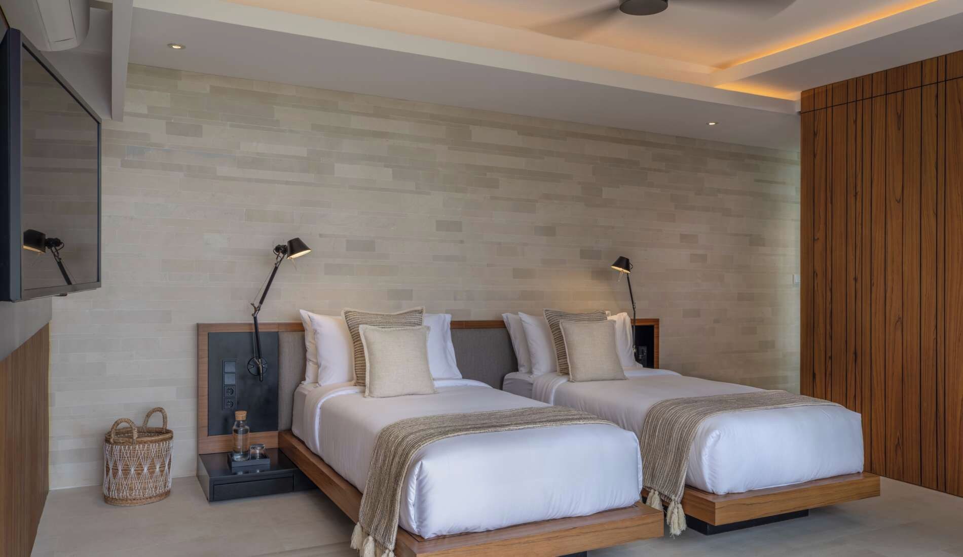 Un dormitorio moderno con dos camas, un televisor montado en la pared y un armario de madera.