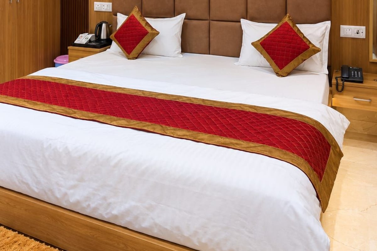 Quarto de hotel com uma cama grande, ventoinha no teto, cabeceira de madeira, luminárias de cabeceira e mesa de cabeceira com telefone e abajur.
