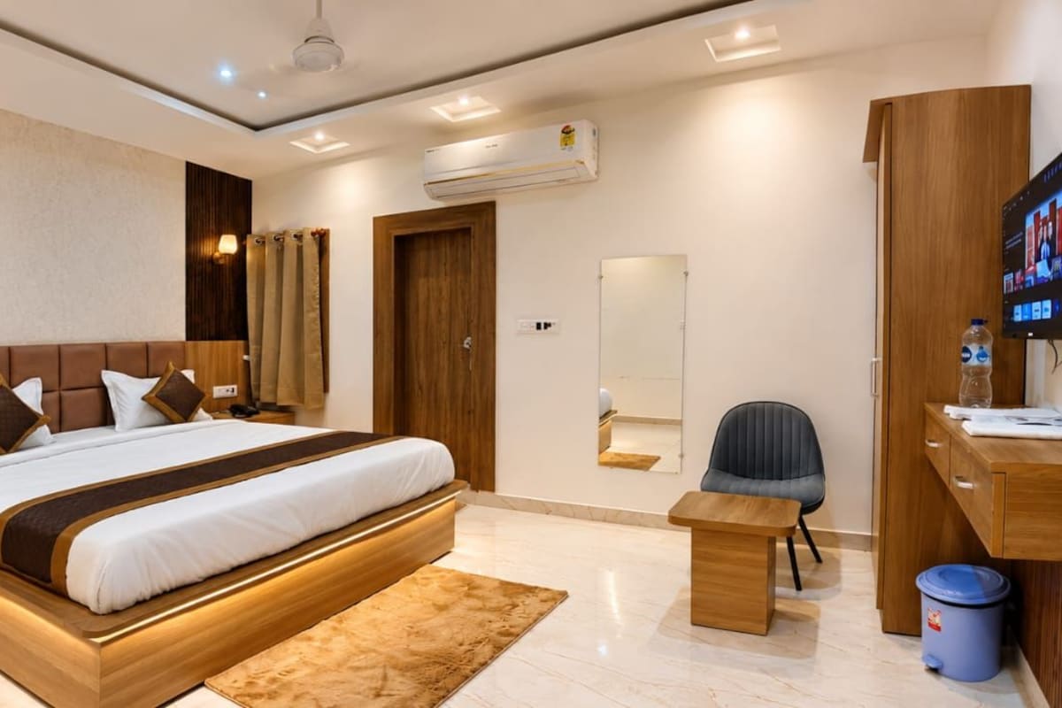 Una habitación de hotel moderna con una cama grande, una mesita de noche, un escritorio con una silla, televisión y un baño con espejo.