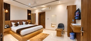 Una habitación de hotel moderna con una cama grande, una mesita de noche, un escritorio con una silla, televisión y un baño con espejo.