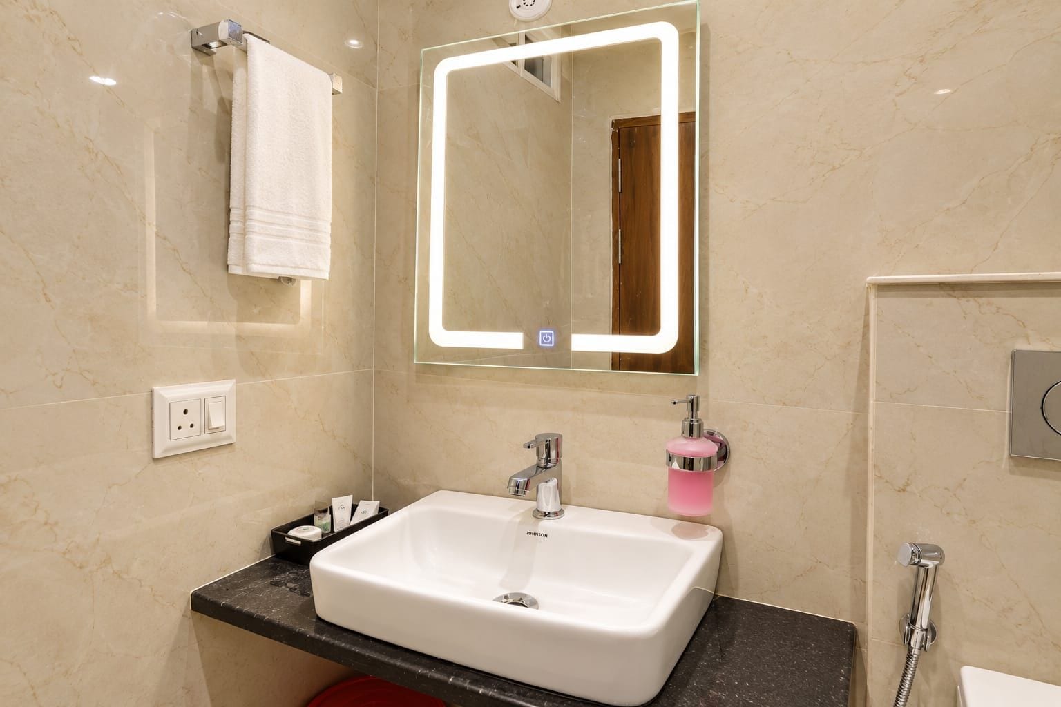 A modern bathroom with a white sink, a mirror with illuminated edges, a towel rack, and a shower area.